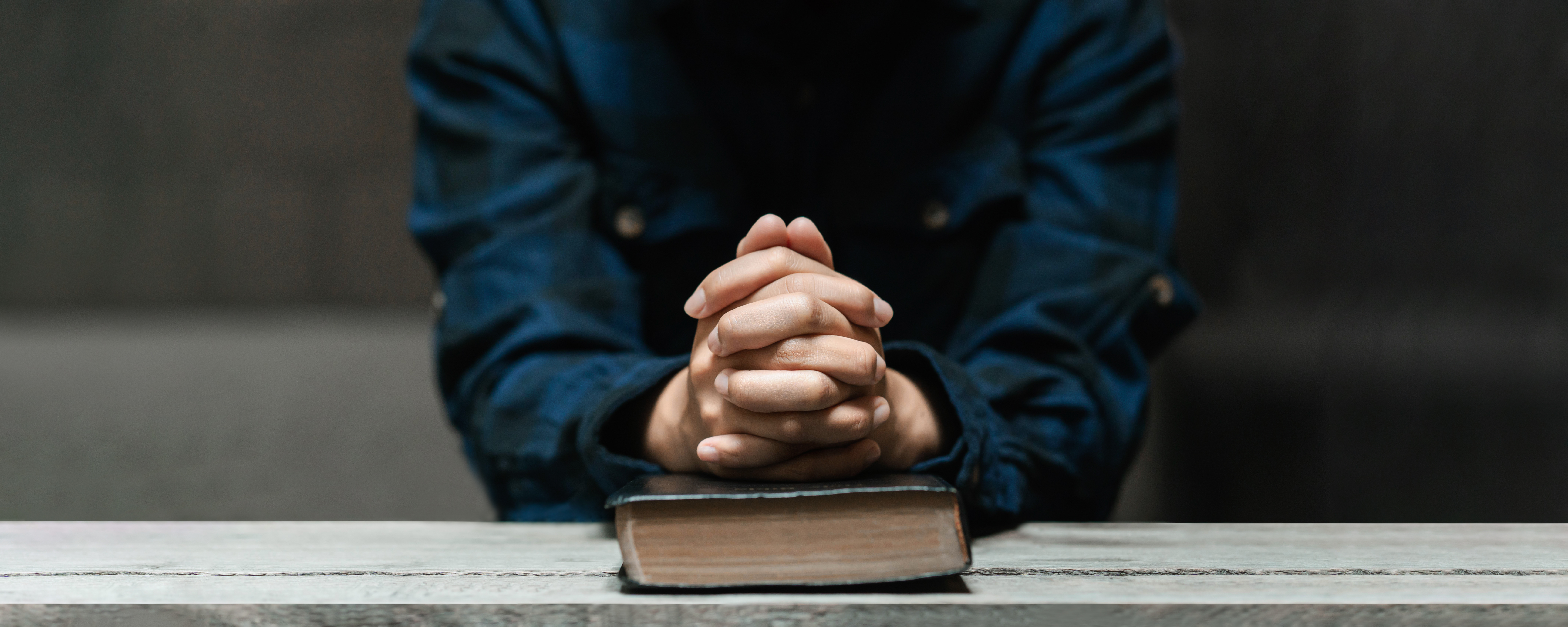 A person with their hands folded in prayer on top of a Bible